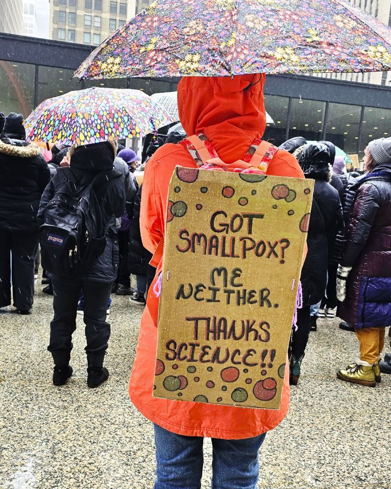 Protester holding an umbrella with a sign on her back that says: Got smallpox? Me neither. Thanks, science!