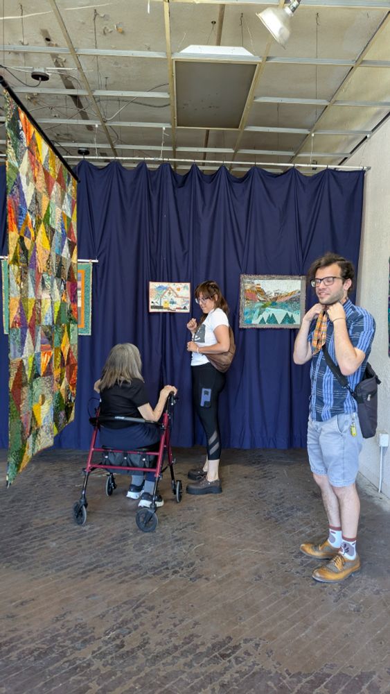 Group of 3 look at quilts in a pop-up exhibition in an unrenovated storefront 
