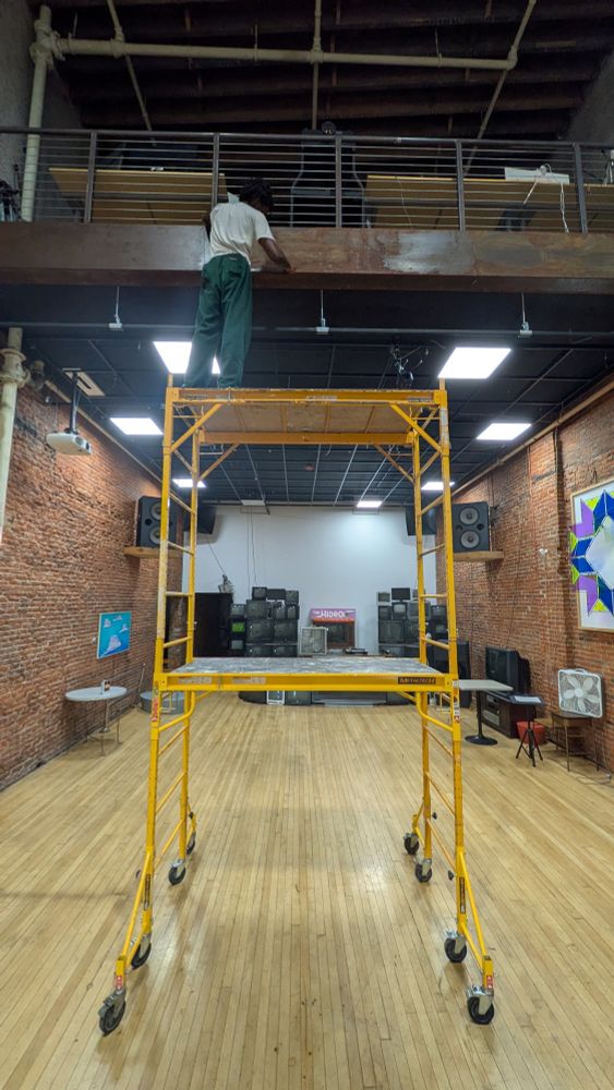 Masc applies rat rod finish to rusty Corten steel facing on mezzanine edge in a large brick room with tube TVs video sculptures