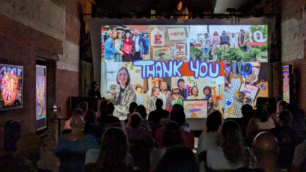 Femme speaker stands at a podium in front of a slide with a collage of photos reads THANK YOU in handwritten bubbly font. A seated crowd is seen in front of the screen; many screens around the room show media artworks in varied styles