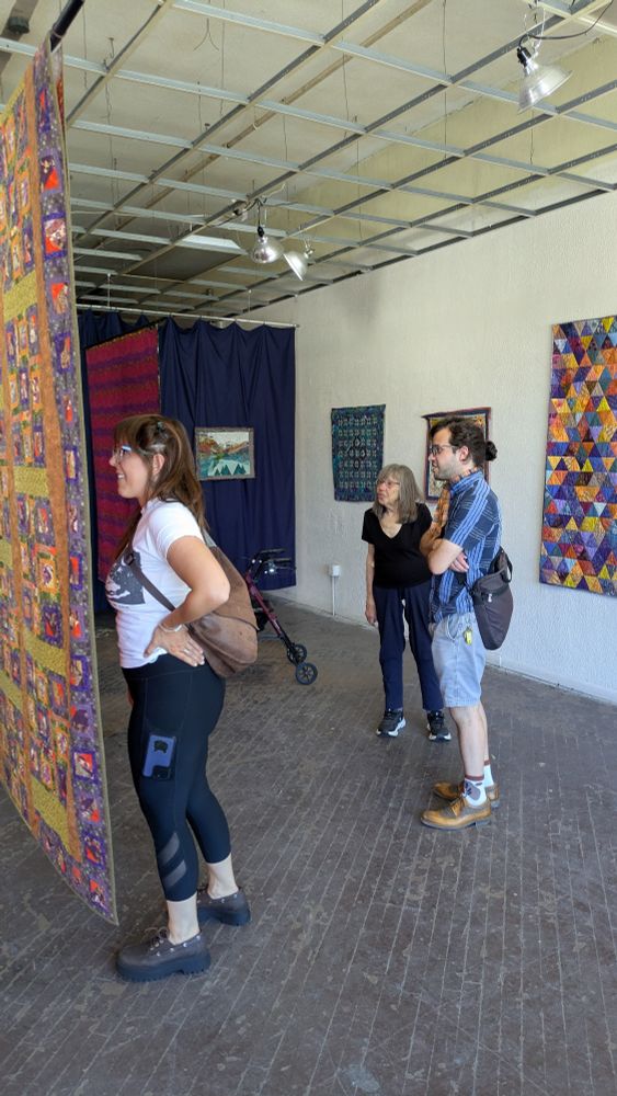 Group of 3 look at quilts in a pop-up exhibition in an unrenovated storefront 