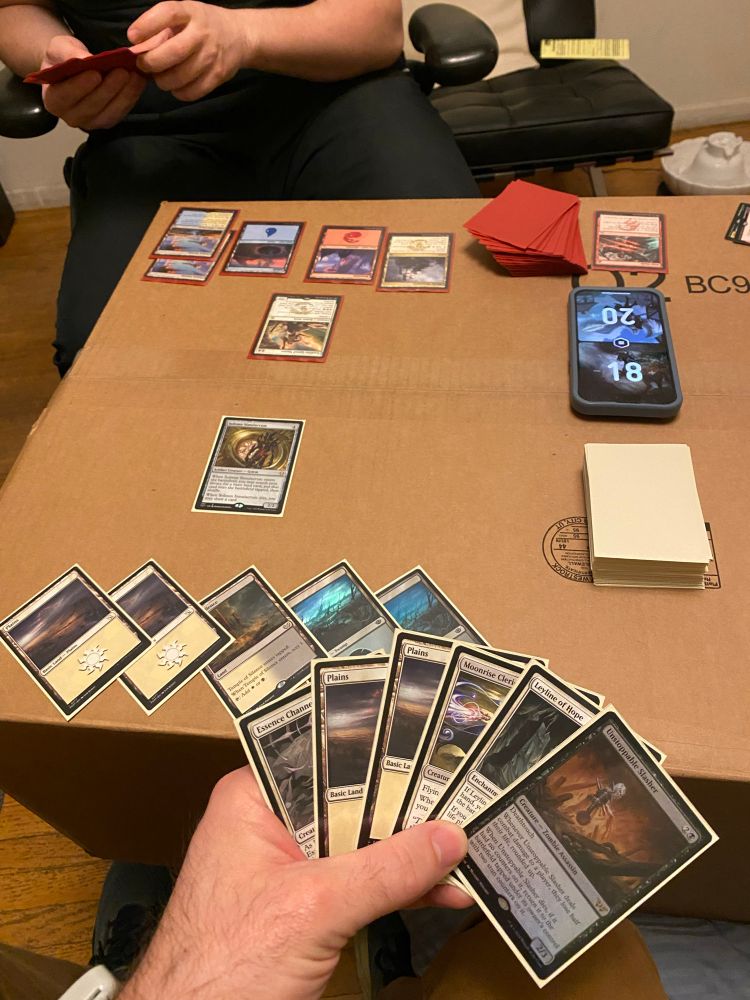 Two people play Magic: The Gathering on a cardboard box