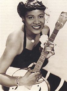 A sepia-toned photo of a young Black woman with a stylish sleeveless dress and a 40s hairstyle adorned with a white flower.