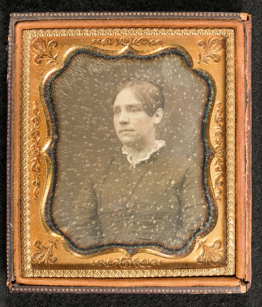 A vintage, sepia-toned picture of a woman in her 40s. The photo is damaged, and has a golden frame.