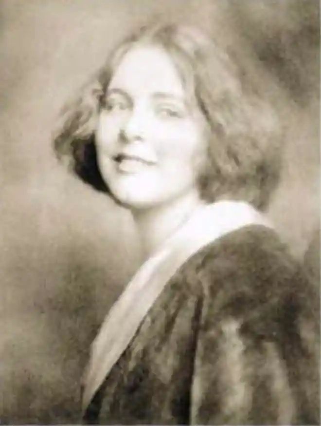 A sepia-toned picture of a young woman smiling. She has short and wavy hair. She is a student, her hair is down, in a casual style.