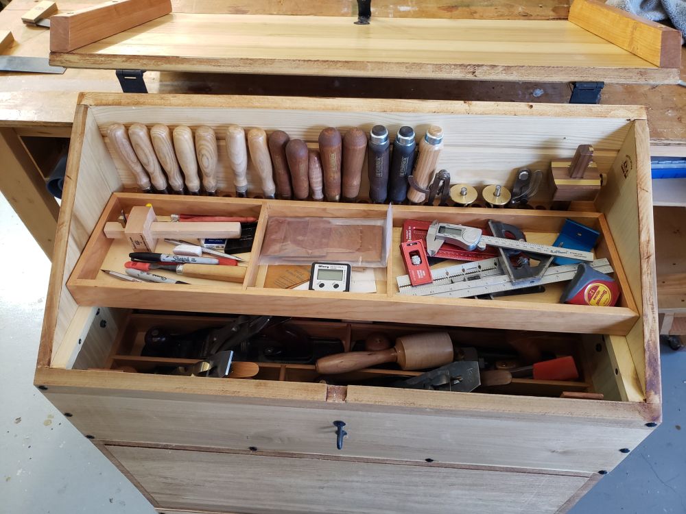 A look into a dutch tool chest without the lid, a sliding tray sits on top, with a row of chisels along the back wall