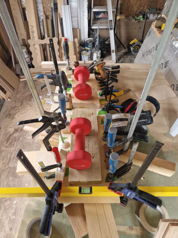 A photo of a piece of oak veneered MDF with a couple dozen clamps, tape and weights keeping it in place while the glue dries