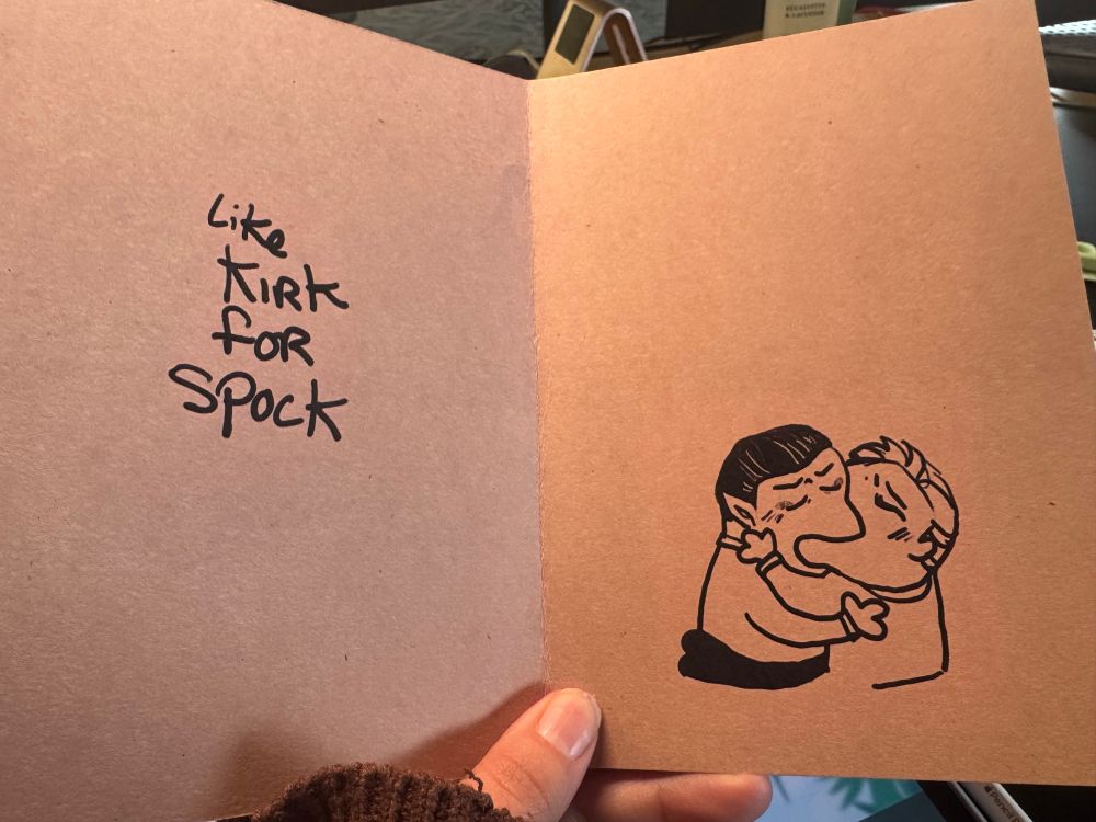 The inside of the card says “like Kirk for Spock” on the left hand side. On the right is a meme doodle of Spock and Kirk kissing sloppy style. Their love is evident and messy. 