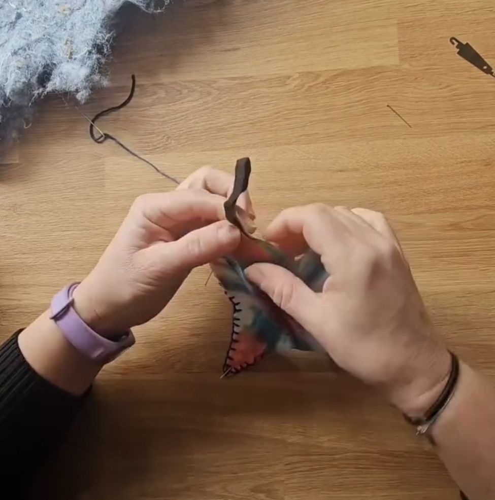 A photograph of two hands sewing and fabric Christmas tree decoration out of tie dye fabric.