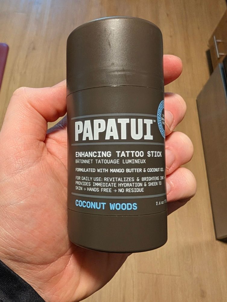 Bottle of a tattoo enhancing stick held in a left hand