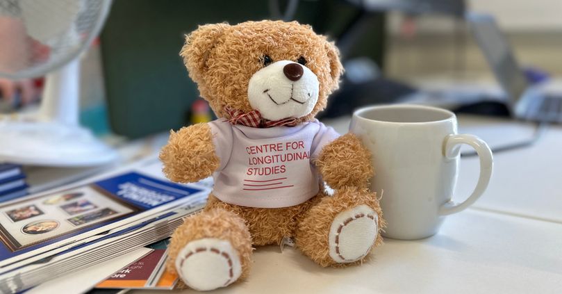 A teddy bear on a desk next to a white mug