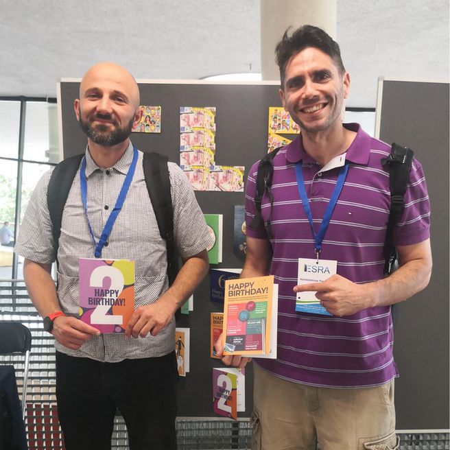 Two men at a conference holding birthday cards
