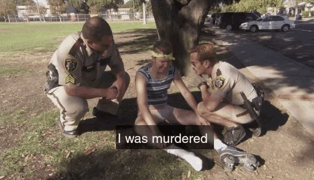 A man is sitting in the ground, crying, with two cops next to him, with the words “I was murdered”