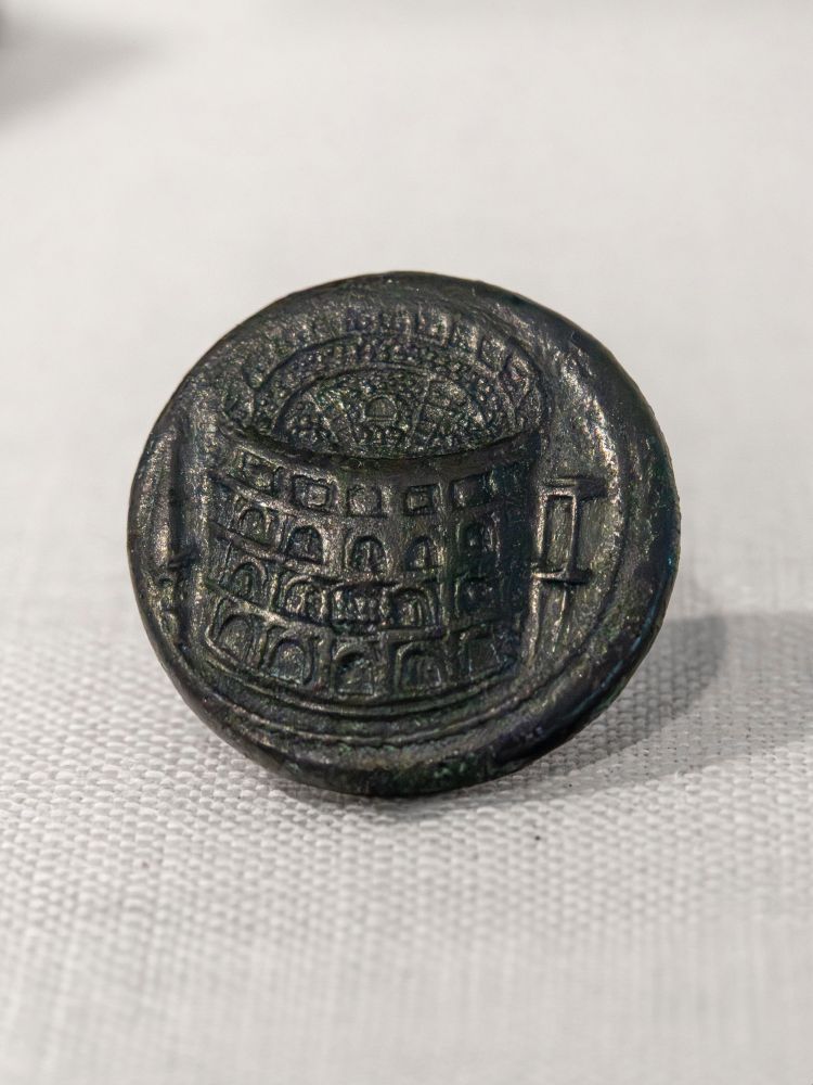 A dark bronze sestertius from the reign of the Roman emperor Titus (79-81 CE), aka Titus Caesar Vespasianus, son of the emperor Vespasian. The coin depicts the Colosseum (Flavian Amphitheatre) in great detail - you can see the four arched stories, statues within the arches, and a two story portico (perhaps a connection between the Colosseum and Titus' baths) on the right side. It even depicts the alternating clypea, the huge circular bronze shields once placed on the cornice of the fourth floor, and in the center - facing us - the gilded quadriga sculpture over the north-east entry. On the left is the large conical monumental fountain - the Meta Sudans - which stood outside the Colosseum until 1936, when Mussolini had it destroyed to create a traffic circle for his fascist parades.