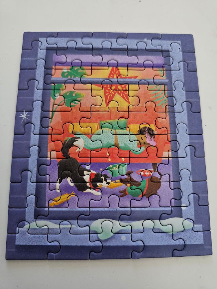 Photo d'un mini puzzle sur fond blanc. Le puzzle représente une fenêtre enneigée au ton orangé par laquelle on aperçoit un intérieur chaleureux avec un enfant qui sort sur un canapé. Au dessus de l'enfant une étoile, et devant le canapé 2 chiens qui jouent.

Le puzzle est un mini puzzle de 50 pièces ce qui laisse paraître de nombreux traits.