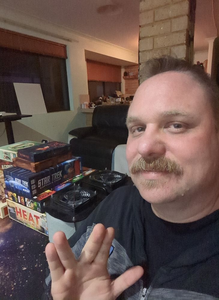 a selfie of me doing the vulcan salute, theres an air filter and a stack of board games behind me 