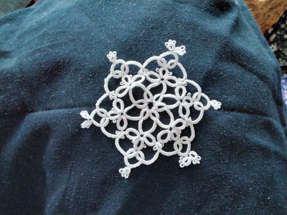 Eine verschnörkelte Spitzen-Schneeflocke liegt auf einem dunklen Tuch.