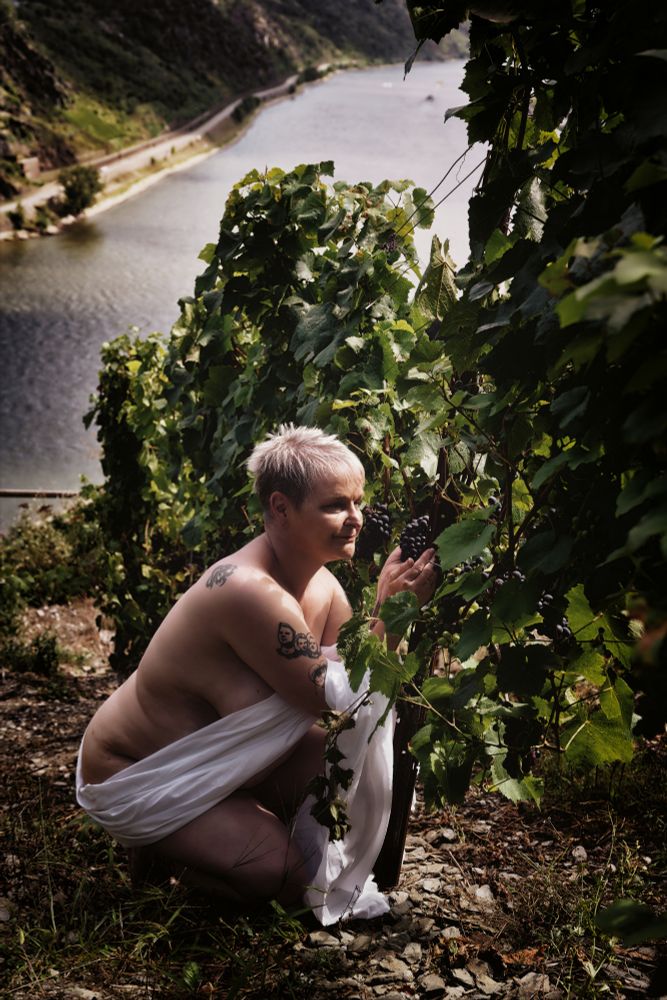 Eine nackte Frau mit einem weissen Tuch in einem Weinberg 
