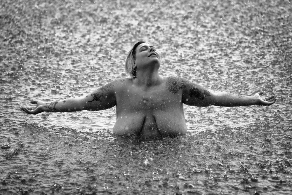 Eine nackte Frau mit ausgebreiteten Armen im Regen in einem See