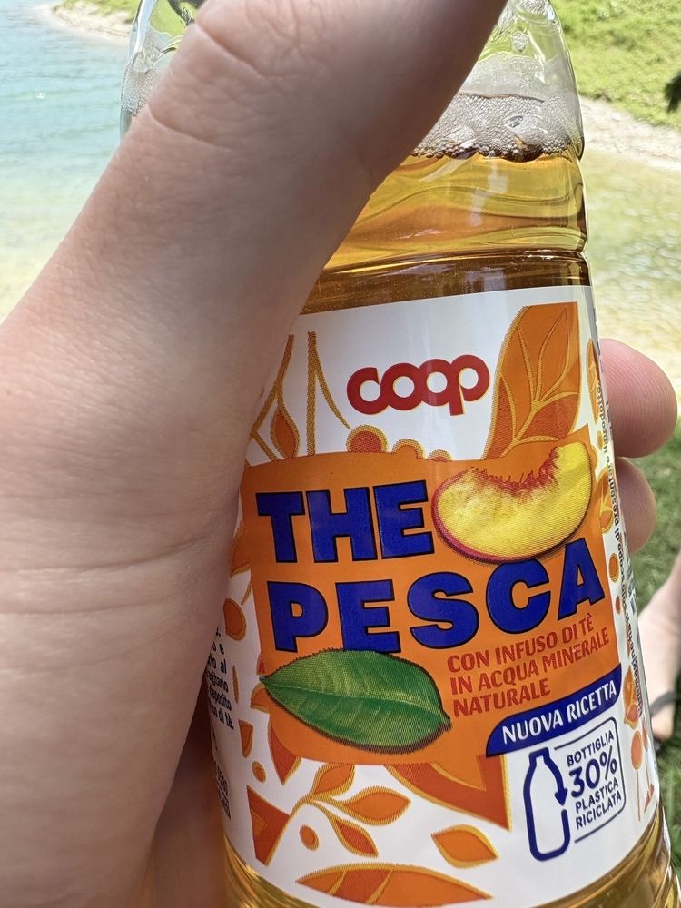 A hand is holding a bottle of COOP peach-flavored drink with vibrant label designs.