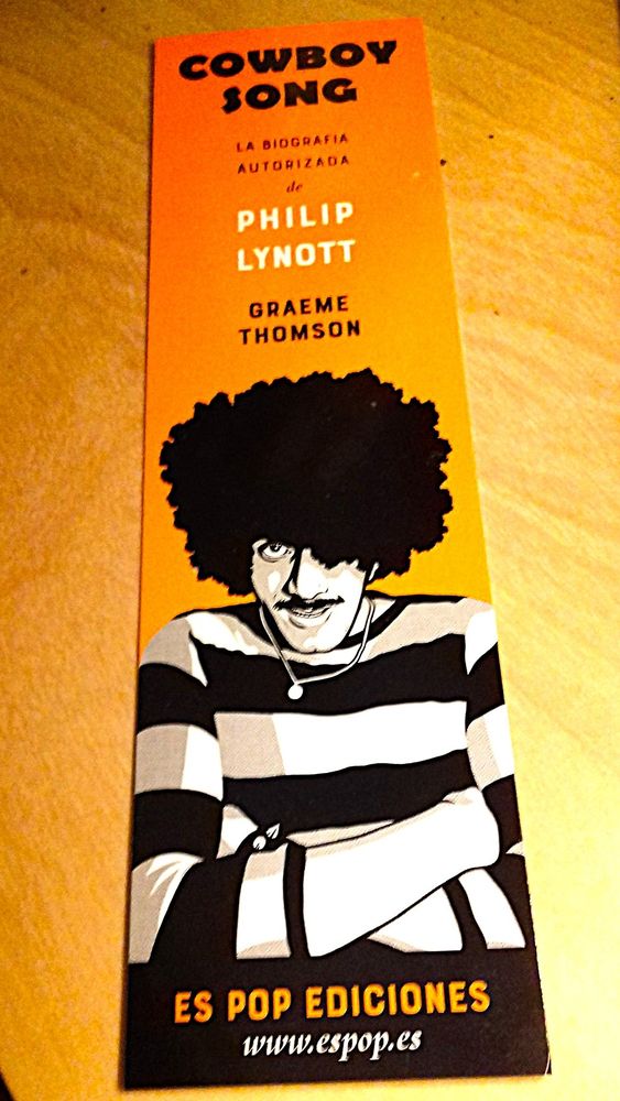 An orange bookmark with a cartoon black and white likeness of Philip Lynott on the bottom half, created for the Spanish edition of Cowboy Song, my 2016 Lynott biography.