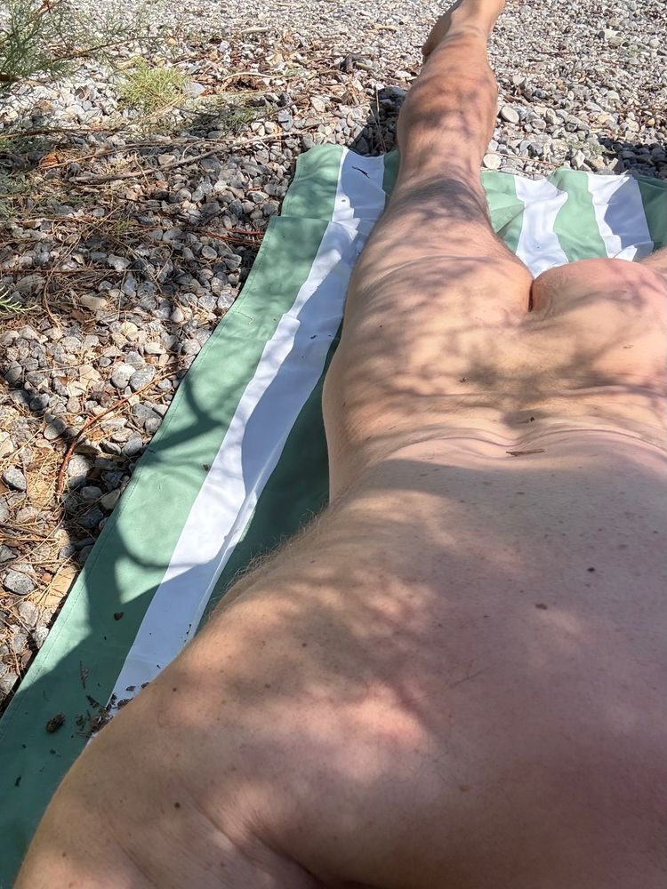 Rear view of a naked man sunbathing on a stony beach 