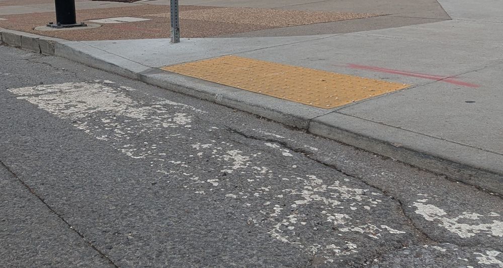 A noncompliant ADA ramp with a large curb lip on the west side of 4th Ave S