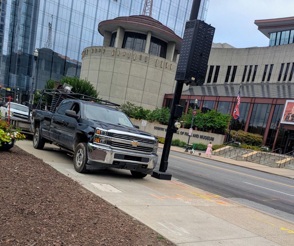 Two giant trucks and one tiny scooter parked on the sidewalk