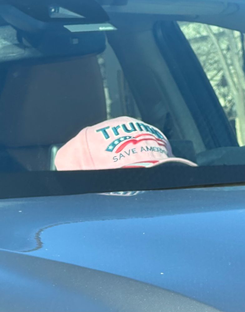 Pink cap with “Trump Save America” printed on it sitting the dashboard of a parked car
