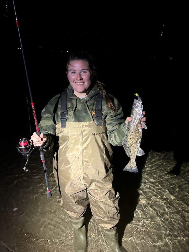 Person in waders holding a fishing rod and a trout. 