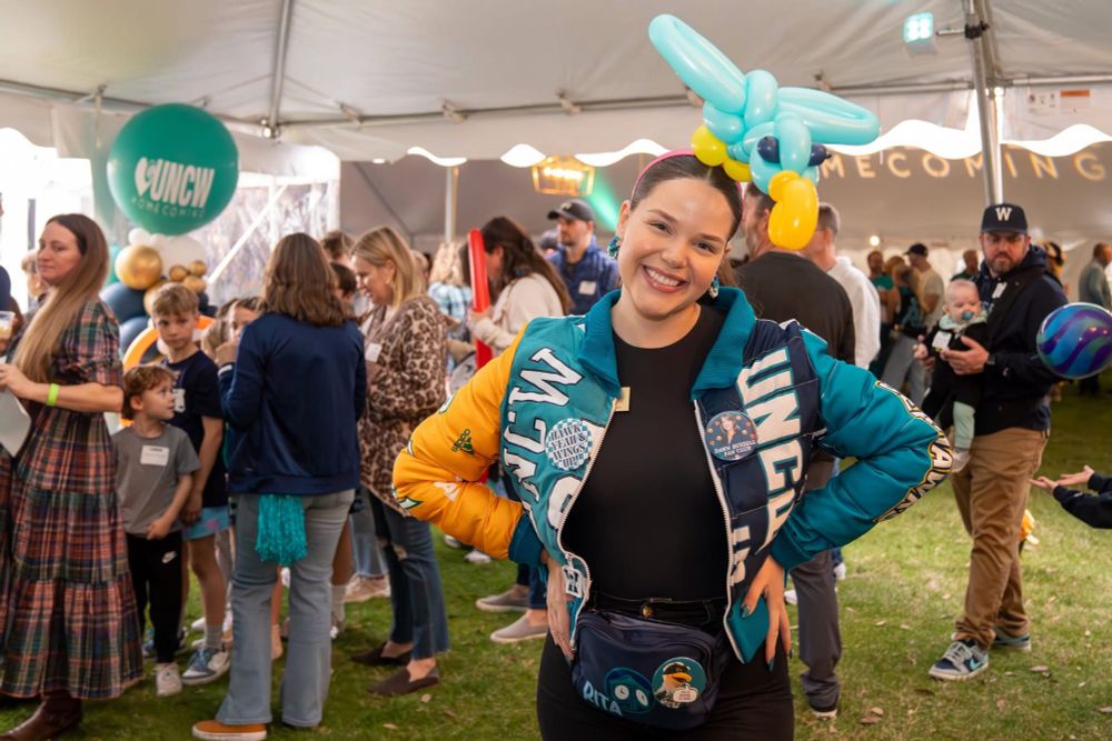 Person with a ballon animal head band standing inside a crowded tent 