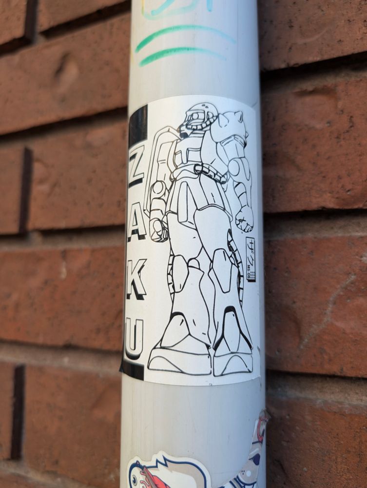 A sticker on a drainage pipe of a Zaku from Gundam with its name printed vertically ok the left.