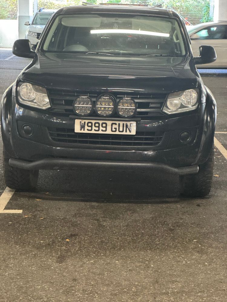 Very large car with spotlights, parked badly with a comically macho number plate