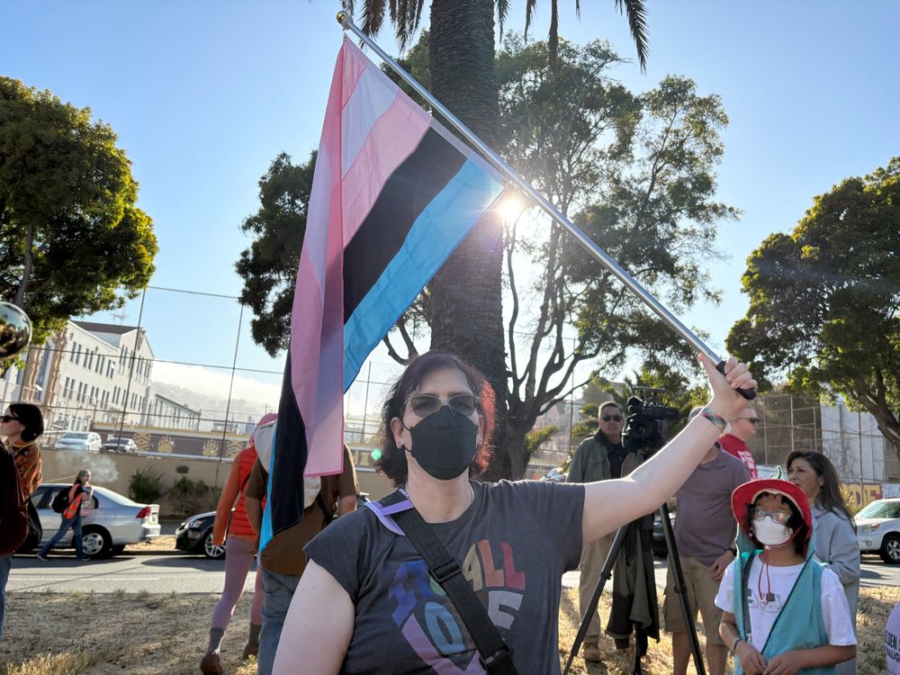 A woman holding up a Dorsey pride flag. It has pink, white, pink, black, and blue stripes. 