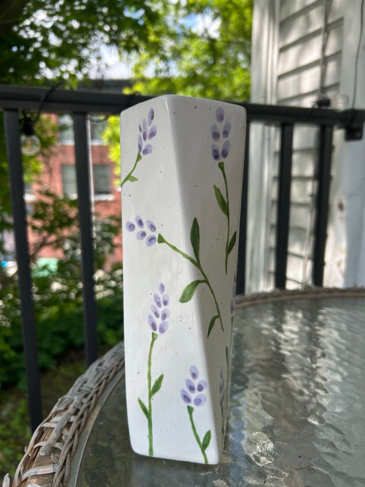 The third side of a white hurricane vase with lavender painted on it. The pieces of lavender vary in size and go in varying directions. Some pieces cross from one side onto another 