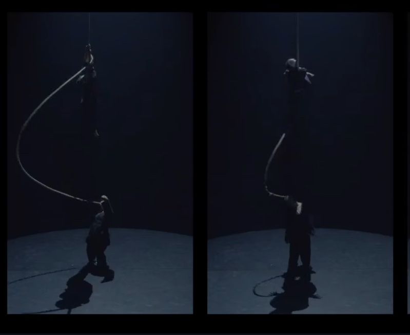 Two performers on stage, one on a rope that’s both attached to the ceiling and woven into the hair of another.