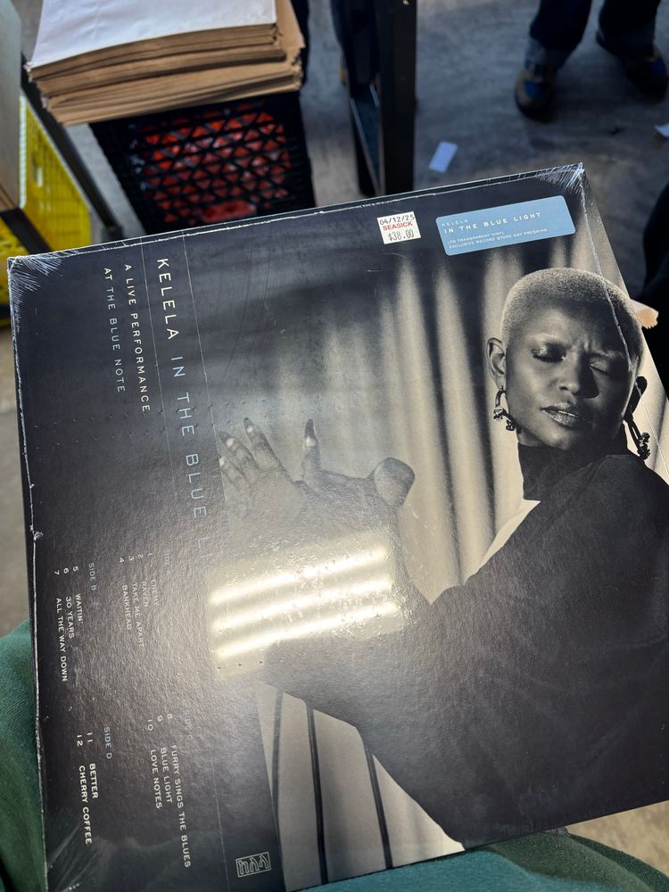  black and white album cover featuring Kelela in a dark colored outfit holding a microphone and her head turned to the side with eyes closed. There is a curtain behind her.