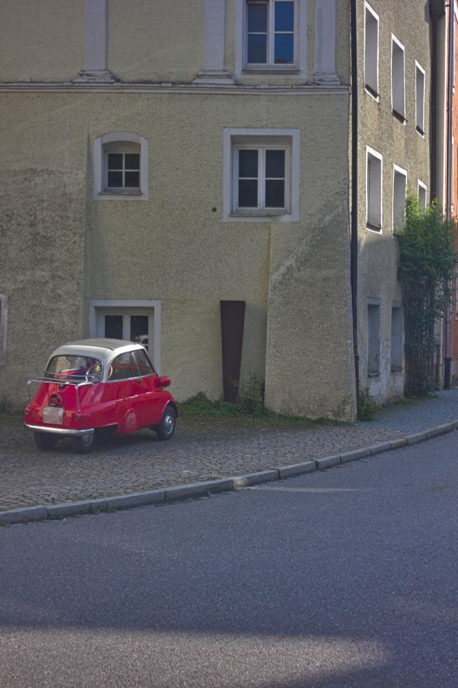ein roter isetta vor der fassade eines alten hauses in der kurve einer alten straße