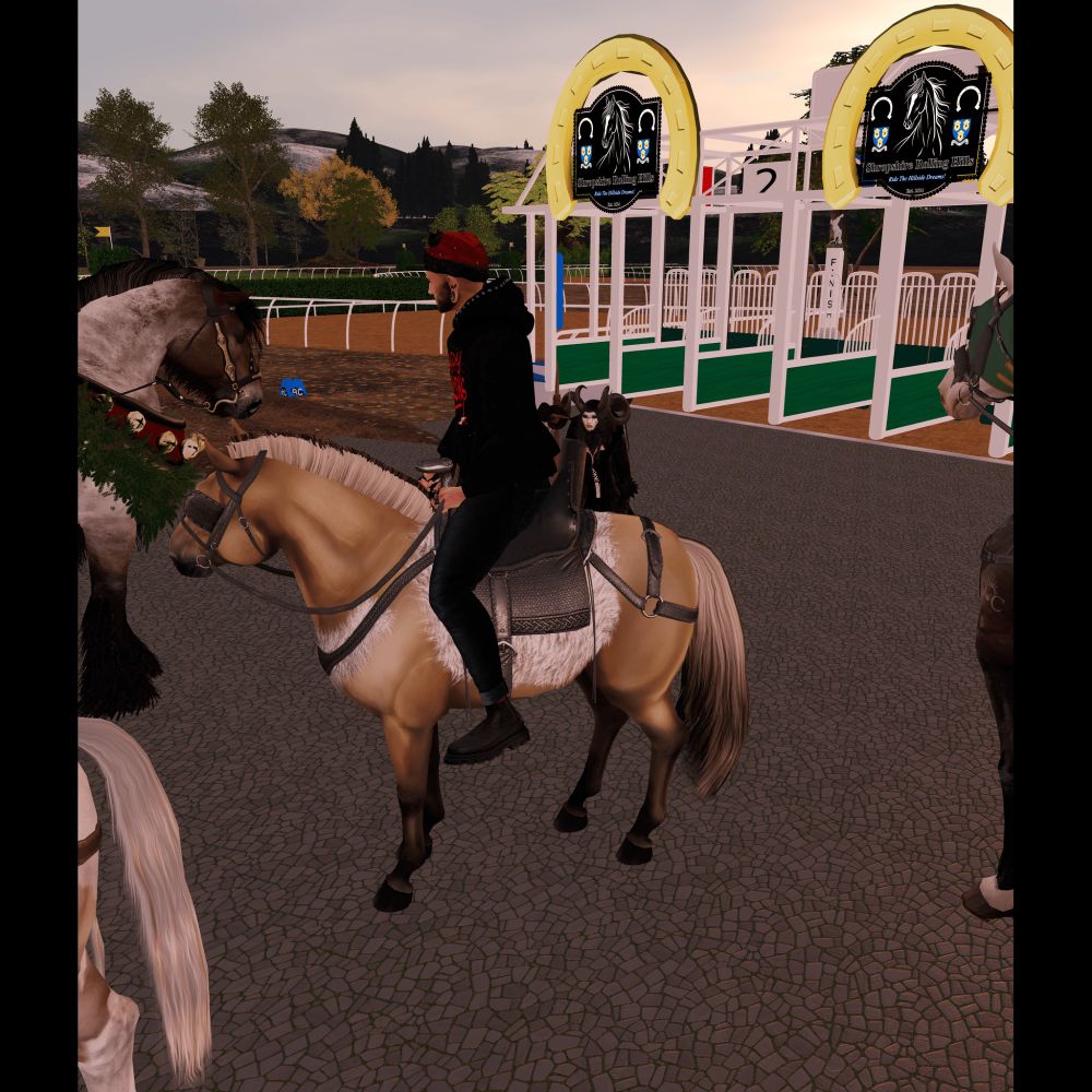 A person wearing a black hoodie, red hat, and black boots is riding a Fjord horse with a light tan coat, dark mane, and a white saddle blanket. The scene is set at what appears to be a horse training or racecourse, with green and white gates in the background featuring horse-themed signs. The environment includes cobblestone pavement, additional horses adorned with festive decorations, and a landscape with trees and rolling hills in the distance under a cloudy sky.
