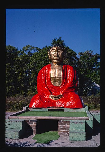 Image shows a (most likely) plaster seated buddha resting on fake grass for a miniature golf hole. His robe is painted bright ruby red with a high gloss finish. His skin is painted gold. Let's just say his face does not follow the standard proportions of Buddhist iconography. 