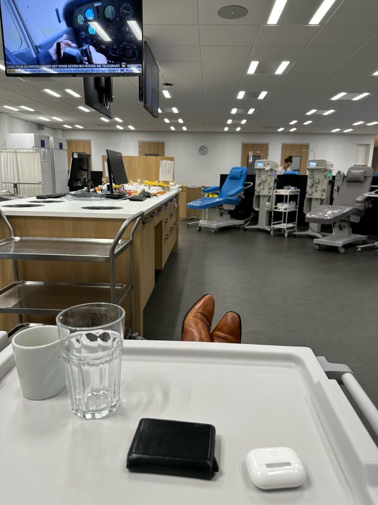 Photo taken in a supine position with a tray and the donor's shoes in the foreground. In the background two chairs where blood donors can lie during collection and on the left a workstation for the blood bank staff.