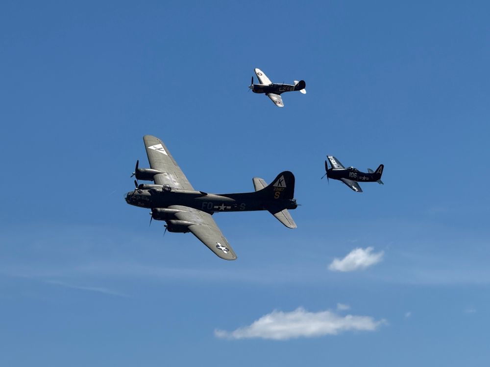 B17 Ye Olde Pub flying formation in front of a P40 and a F8F. Light clouds in otherwise blue skies. 