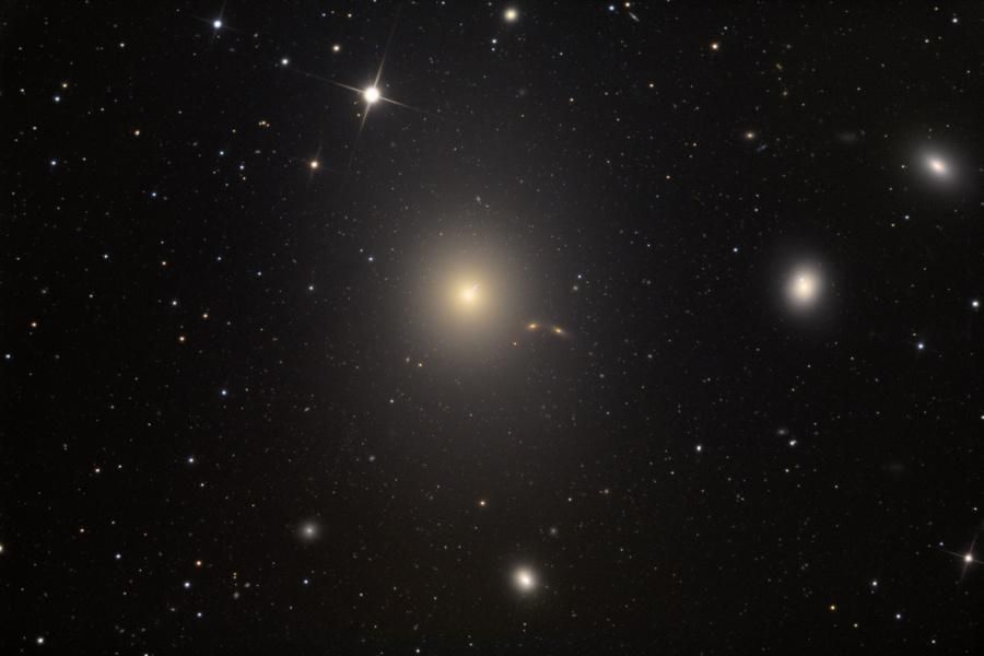 A telescopic view of the giant elliptical galaxy M87 (NGC 4486), the dominant galaxy in the Virgo Cluster.  M87, over 120,000 light-years across, is larger than our Milky Way and contains a supermassive black hole,  producing a high-energy jet visible near the one o'clock position.  Other galaxies, including NGC 4478 and NGC 4476, are also visible in this deep-space image.