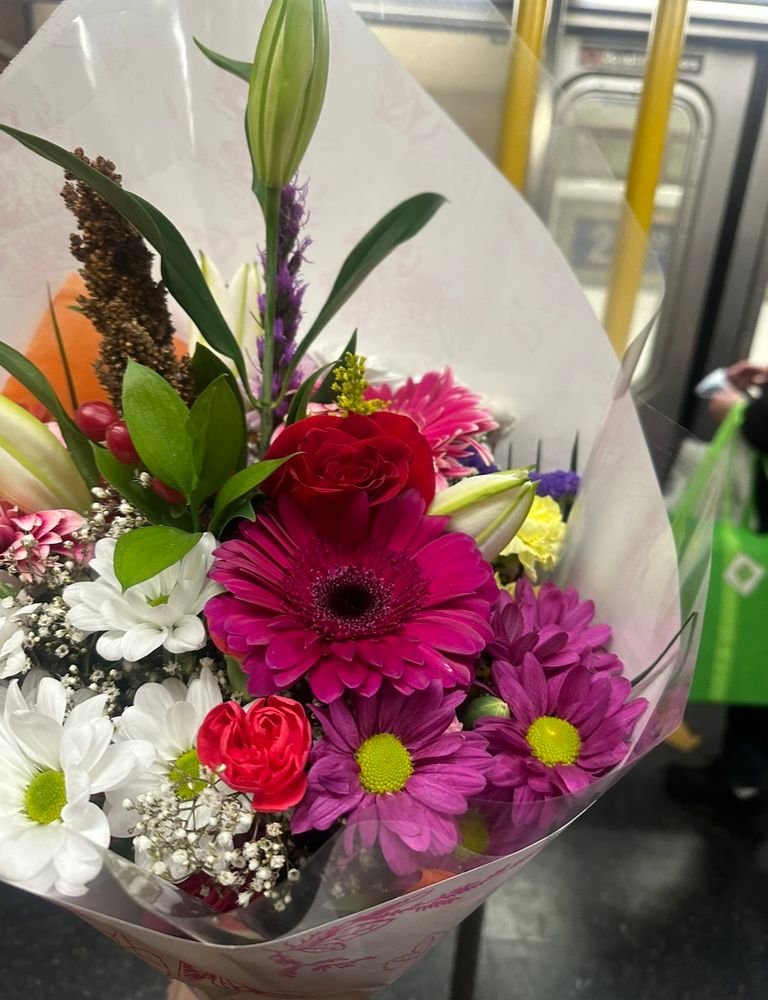 A large bouquet of flowers being held up on the subway. There are white, pink, purple, yellow and red flowers.