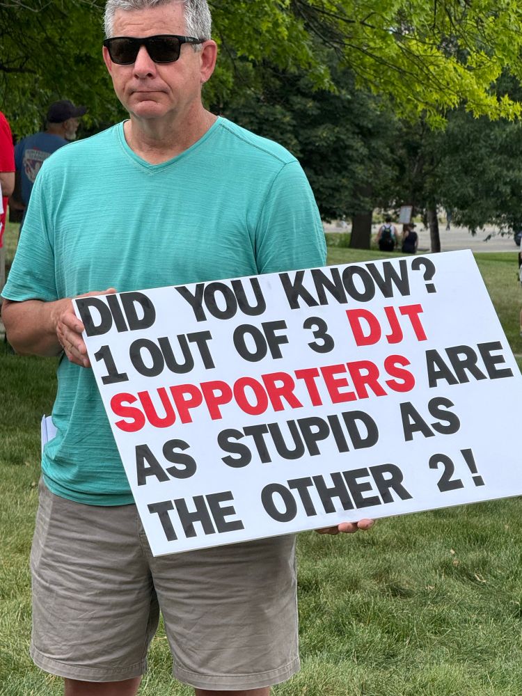 Guy holding sign reading “ Did you know that 1 out of 3 DJT supporters are as stupid as the other 2!