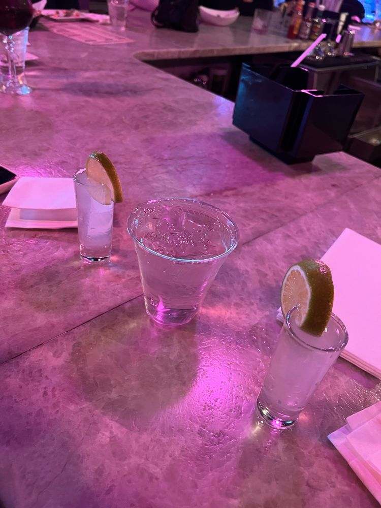 Two tequila shots on a marble bar with plastic cup of water between 