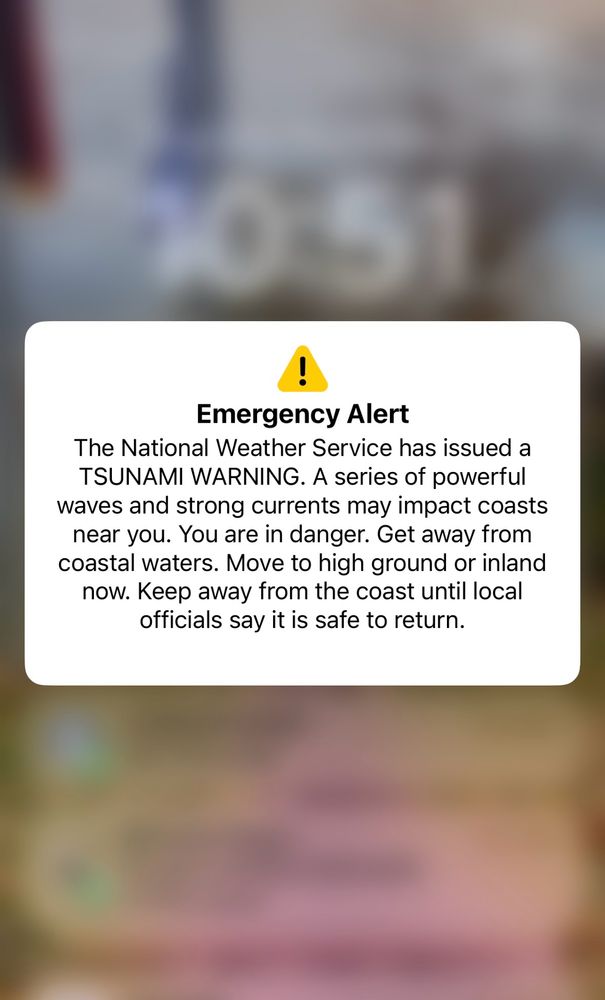 Screenshot of an emergency alert on an iPhone which reads: The National Weather Service has issued a TSUNAMI WARNING. A series of powerful waves and strong currents may impact coasts near you. You are in danger. Get away from coastal waters. Move to high ground or inland now. Keep away from the coast until local officials say it is safe to return.