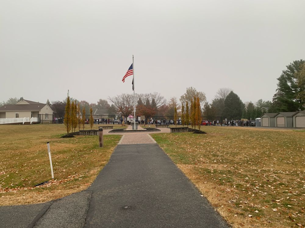 American flag flying in foreground with voters in line in the background. 