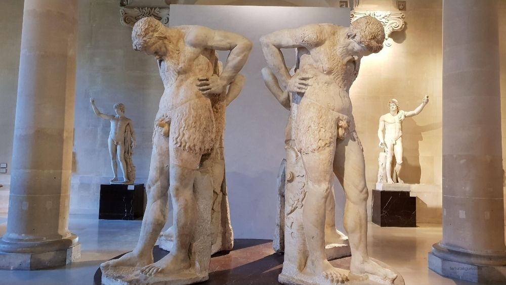 Two statues of naked men, staring at their penises, as though they were once supporting a building on their shoulders 