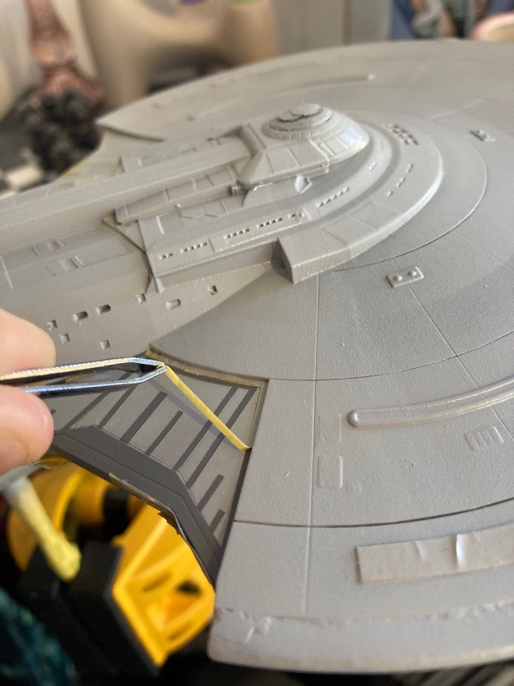 Peeling off masking tape to reveal darker grey paint on a grey 1/1400 USS Enterprise G model. The contrast is a bit higher than I expected, but I should be able to bring that down with a blending coat at a later stage.